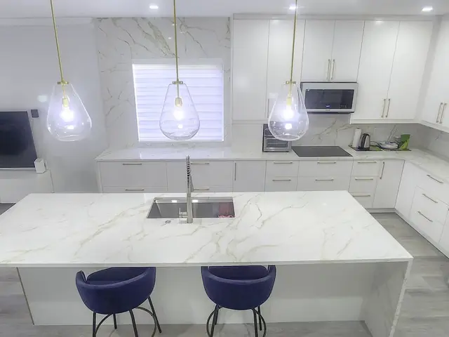 White kitchen with a marble island and glass pendants